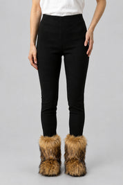 Bottes en moumoute marron portées avec un pantalon noir, vue de face sur fond gris clair.