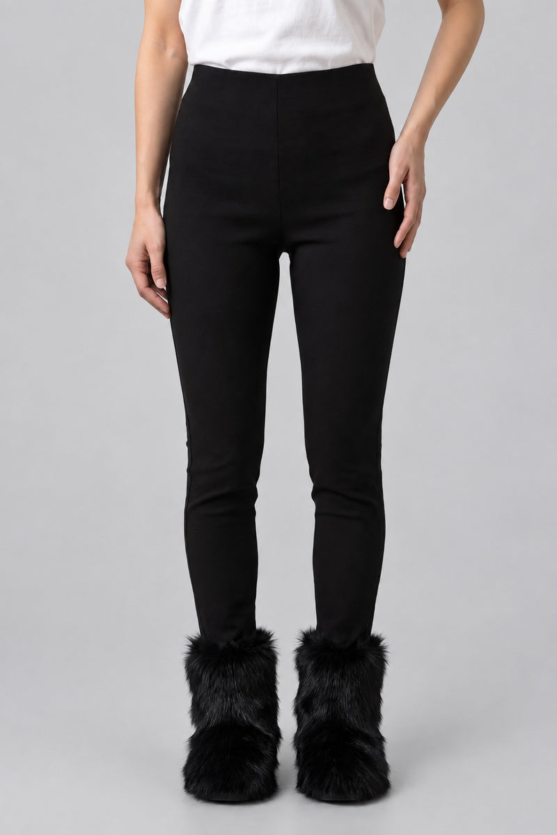 Bottes en moumoute noires portées avec un pantalon noir, vue de face sur fond gris clair.