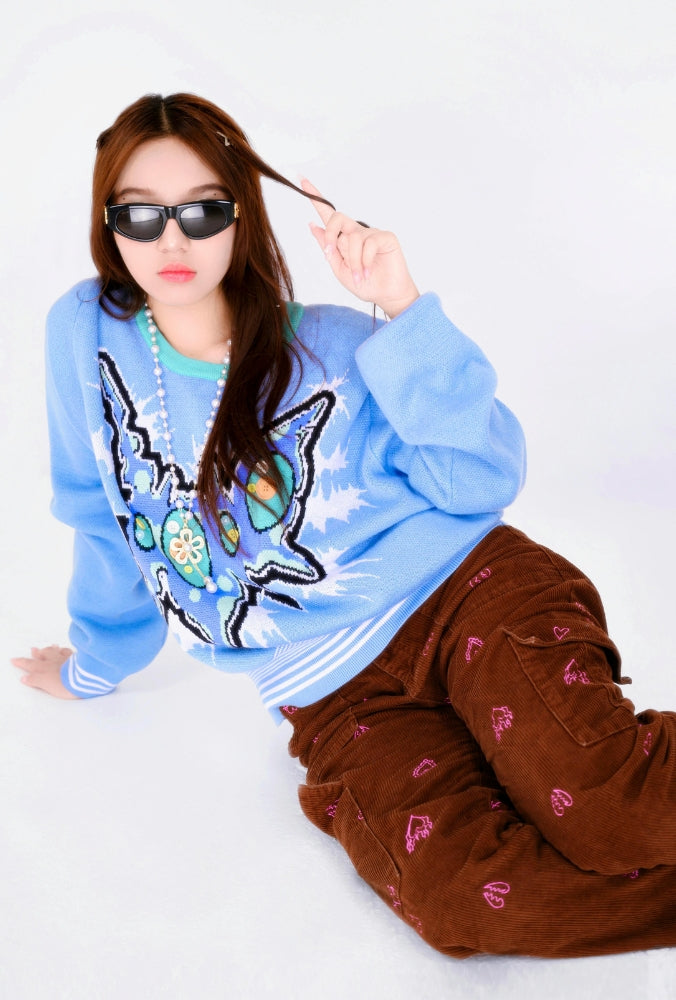 Femme portant un pull bleu illustré style Y2K avec un pantalon cargo marron décoré de motifs roses.