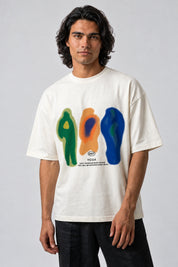 T-shirt écru oversize avec trois silhouettes graphiques verte, orange et bleue, porté de face.