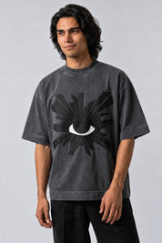 T-shirt gris oversize avec grand œil blanc entouré de rayons noirs en relief, vue de face.