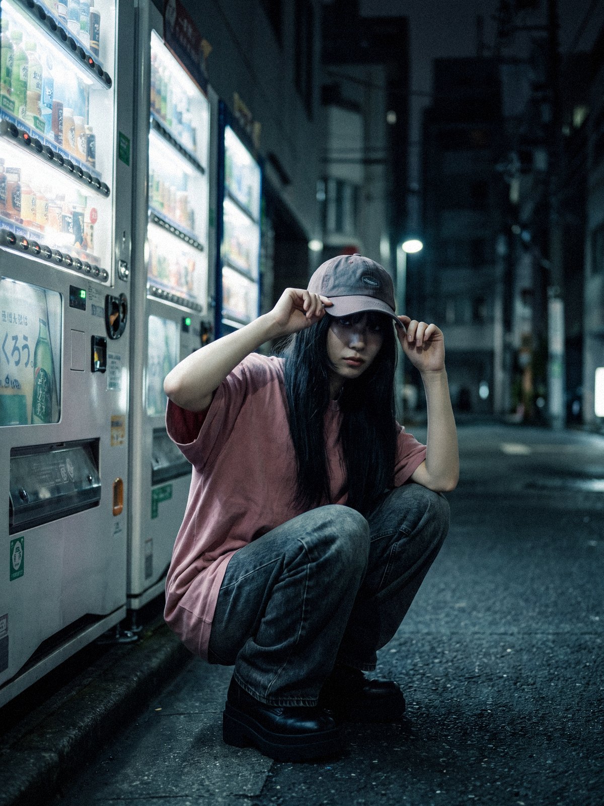 Jeune femme en tee-shirt oversize et jean baggy accroupie devant des distributeurs la nuit – Notre marque Y2K | Y2K Club